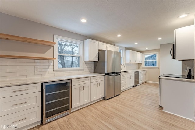 kitchen with wine cooler, sink, light hardwood / wood-style flooring, appliances with stainless steel finishes, and white cabinets