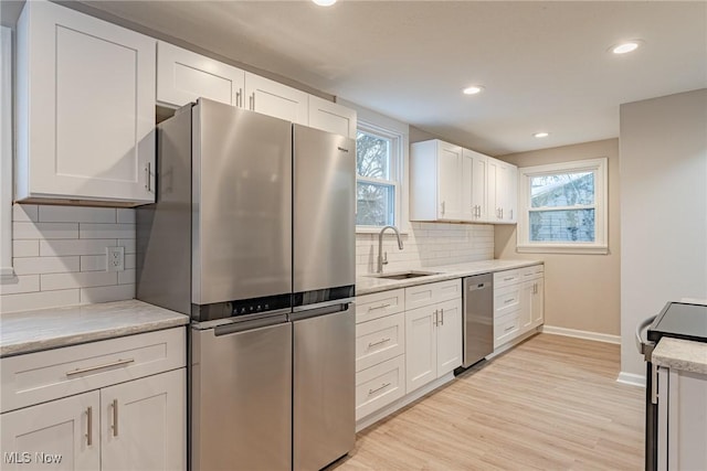 kitchen featuring appliances with stainless steel finishes, white cabinetry, tasteful backsplash, light hardwood / wood-style floors, and sink