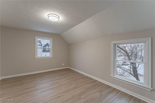 additional living space with a textured ceiling, lofted ceiling, and light wood-type flooring