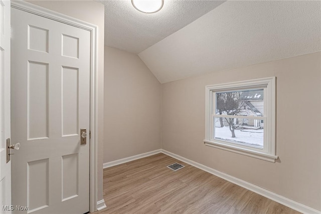 bonus room with light wood-type flooring, vaulted ceiling, and a textured ceiling