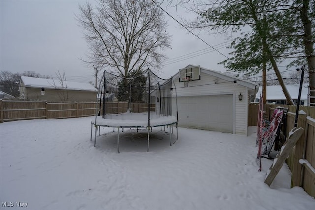 yard layered in snow featuring a trampoline, a garage, and an outbuilding