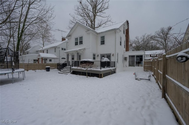 snow covered rear of property with a trampoline and a wooden deck