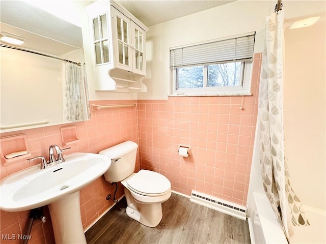 full bathroom with toilet, hardwood / wood-style floors, shower / tub combo with curtain, a baseboard radiator, and tile walls