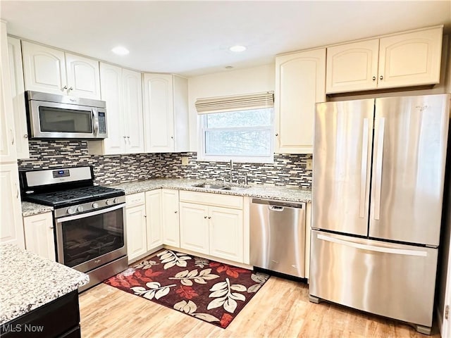 kitchen featuring stainless steel appliances, tasteful backsplash, light hardwood / wood-style floors, sink, and light stone counters