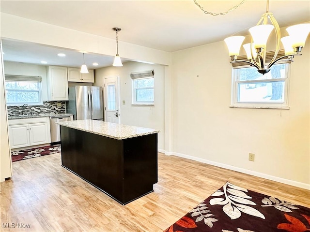 kitchen with decorative backsplash, appliances with stainless steel finishes, white cabinetry, and pendant lighting