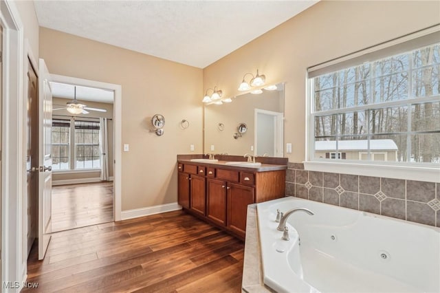 bathroom featuring hardwood / wood-style flooring, ceiling fan, tiled tub, and vanity