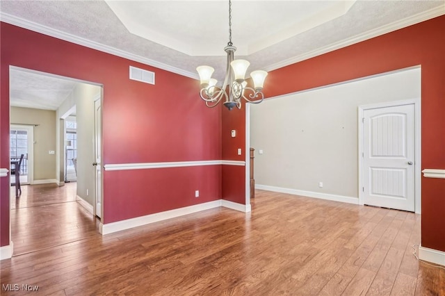 spare room featuring hardwood / wood-style floors, crown molding, a raised ceiling, and an inviting chandelier