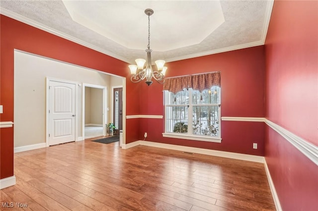 unfurnished dining area with hardwood / wood-style floors, a raised ceiling, a textured ceiling, a chandelier, and crown molding