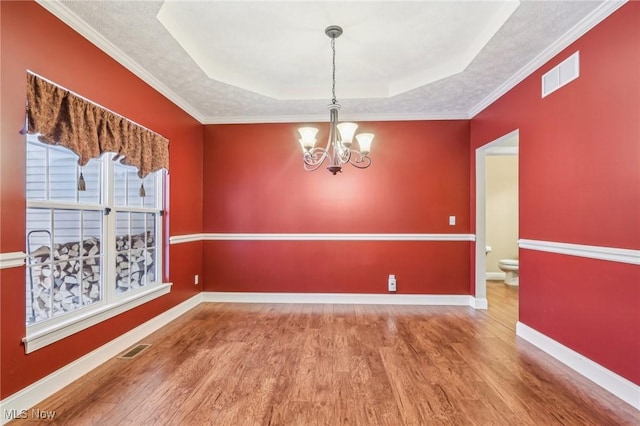 unfurnished dining area featuring crown molding, an inviting chandelier, a tray ceiling, and hardwood / wood-style floors