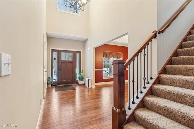 entrance foyer with wood-type flooring, a towering ceiling, and a notable chandelier