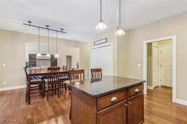 kitchen with wood-type flooring, hanging light fixtures, a center island, and dark stone counters