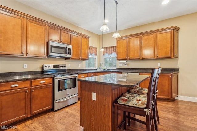 kitchen with appliances with stainless steel finishes, a center island, light wood-type flooring, a kitchen breakfast bar, and sink