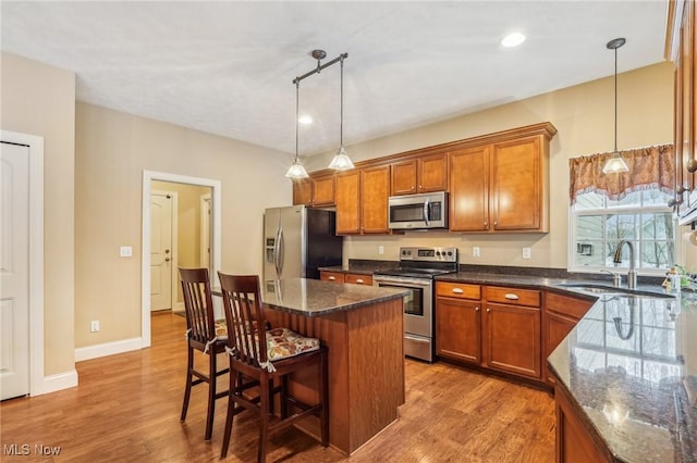 kitchen with appliances with stainless steel finishes, pendant lighting, light hardwood / wood-style flooring, a breakfast bar, and sink