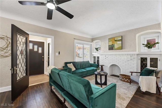 living room with a brick fireplace, a textured ceiling, dark hardwood / wood-style flooring, and ceiling fan