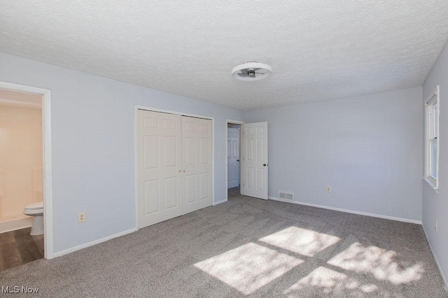 unfurnished bedroom featuring carpet floors, a textured ceiling, a closet, and ensuite bath