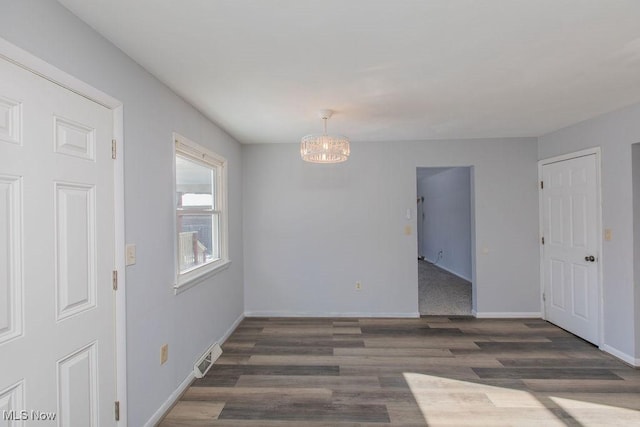 empty room with dark wood-type flooring and an inviting chandelier