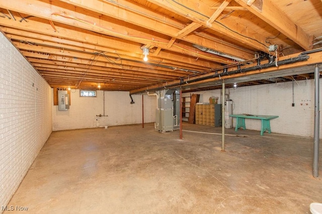 basement with brick wall, electric panel, heating unit, and water heater