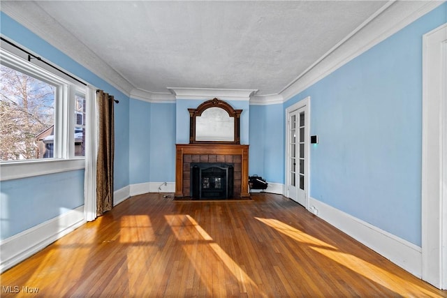 unfurnished living room with baseboards, wood finished floors, crown molding, and a tile fireplace