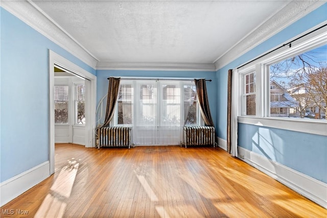 unfurnished room featuring plenty of natural light, radiator heating unit, and hardwood / wood-style flooring