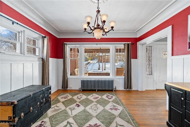 dining space with a wainscoted wall, wood finished floors, radiator heating unit, an inviting chandelier, and crown molding