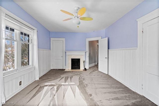 unfurnished living room with a ceiling fan, carpet flooring, a fireplace, and wainscoting