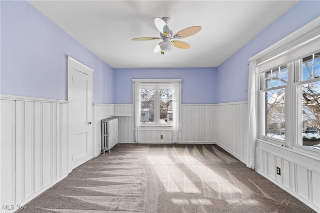 unfurnished room featuring a wainscoted wall, radiator heating unit, a ceiling fan, and carpet floors