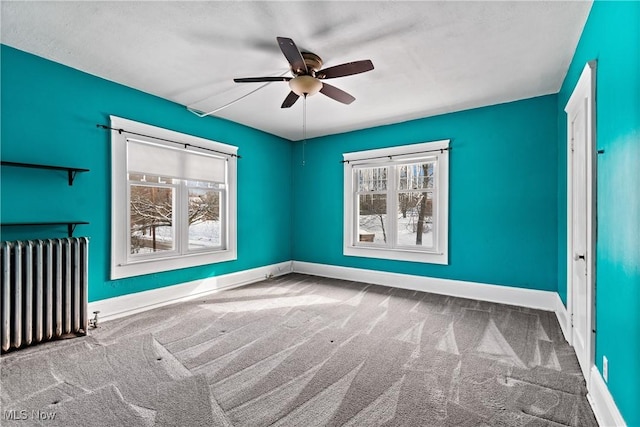 empty room featuring radiator, carpet, baseboards, and a wealth of natural light