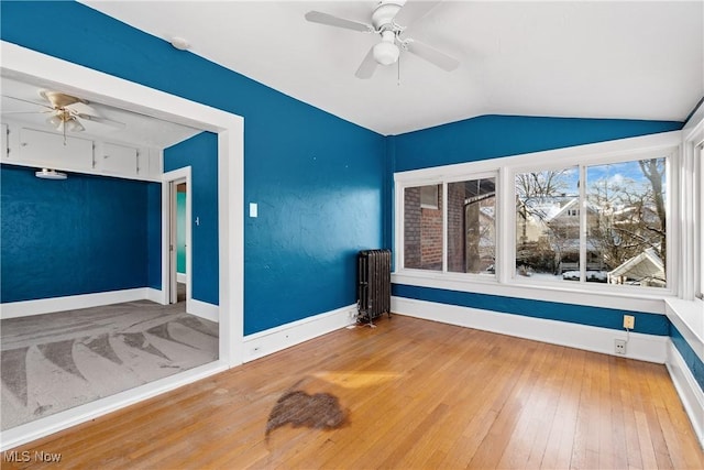 unfurnished room with a ceiling fan, radiator heating unit, wood-type flooring, baseboards, and vaulted ceiling