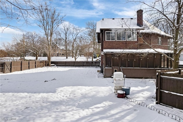 snow covered rear of property with fence, brick siding, and a sunroom