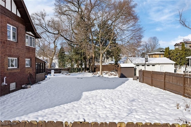 snowy yard featuring an outbuilding, a storage unit, and a fenced backyard