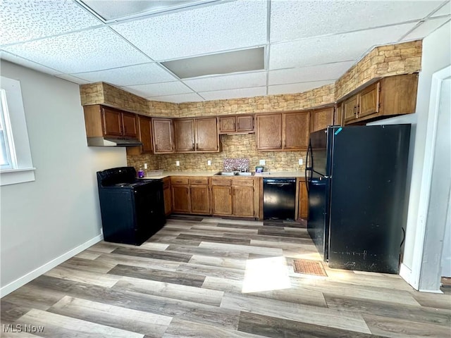 kitchen with light hardwood / wood-style floors, backsplash, black appliances, and a paneled ceiling