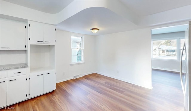 kitchen with white cabinets, stainless steel fridge, a wealth of natural light, and light hardwood / wood-style flooring