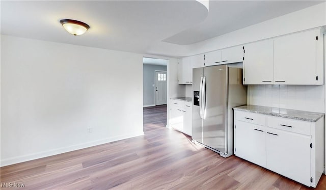 kitchen featuring white cabinetry, stainless steel fridge, backsplash, light wood-type flooring, and light stone countertops