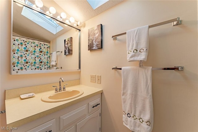 bathroom with vaulted ceiling with skylight, a textured ceiling, and vanity