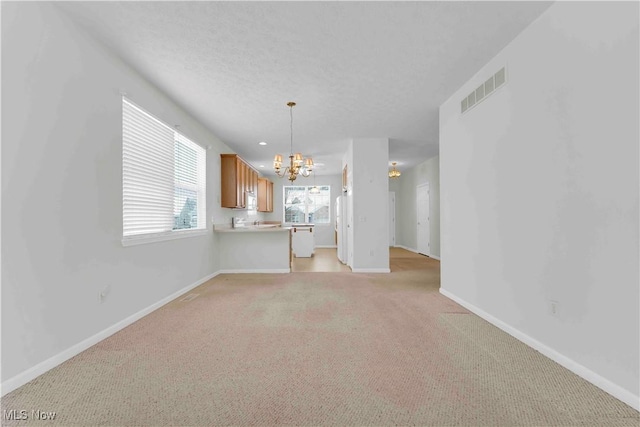 unfurnished living room with a textured ceiling, light carpet, and an inviting chandelier