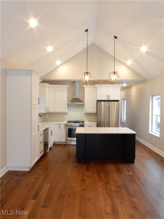 kitchen featuring appliances with stainless steel finishes, decorative light fixtures, wall chimney range hood, a kitchen island, and white cabinets