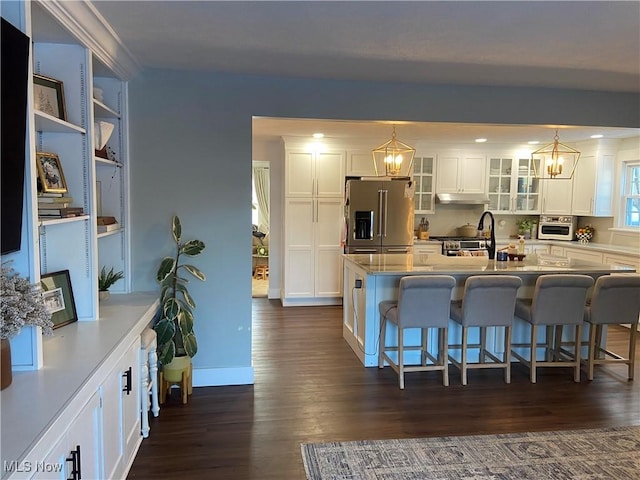 kitchen with a kitchen bar, a center island with sink, stainless steel appliances, decorative light fixtures, and white cabinets