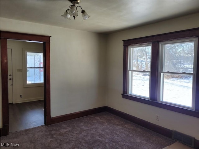 empty room with dark carpet and an inviting chandelier