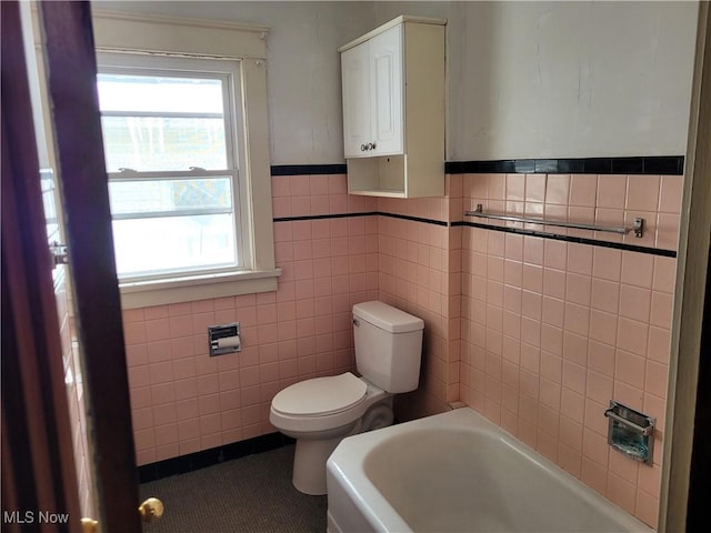 bathroom with tile walls, tile patterned flooring, a washtub, and toilet