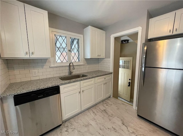 kitchen with light stone countertops, appliances with stainless steel finishes, white cabinetry, decorative backsplash, and sink