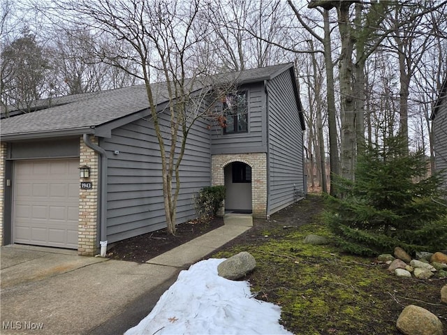 view of front of property with an attached garage, a shingled roof, concrete driveway, and brick siding