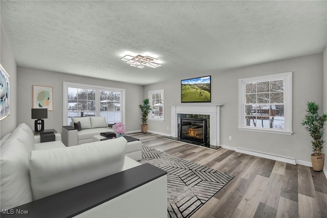 living room with a baseboard heating unit, light wood-type flooring, a fireplace, and a textured ceiling