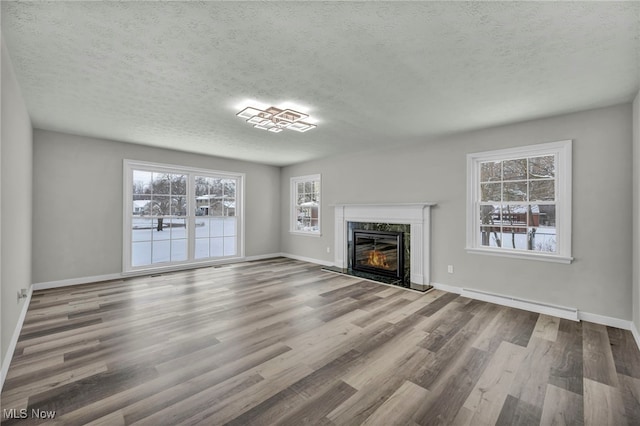 unfurnished living room with a premium fireplace, a baseboard heating unit, hardwood / wood-style floors, and a textured ceiling