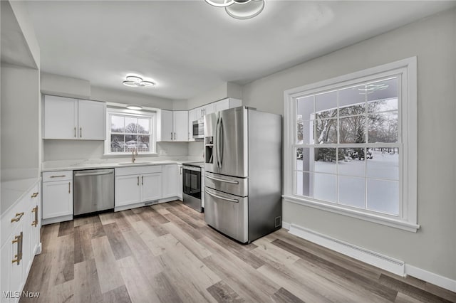 kitchen featuring sink, light hardwood / wood-style flooring, a baseboard heating unit, stainless steel appliances, and white cabinets