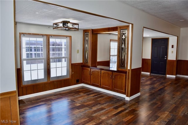 unfurnished dining area with dark wood-type flooring and wood walls