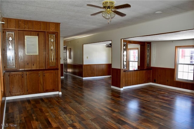 empty room with dark wood-type flooring, ceiling fan, and wood walls