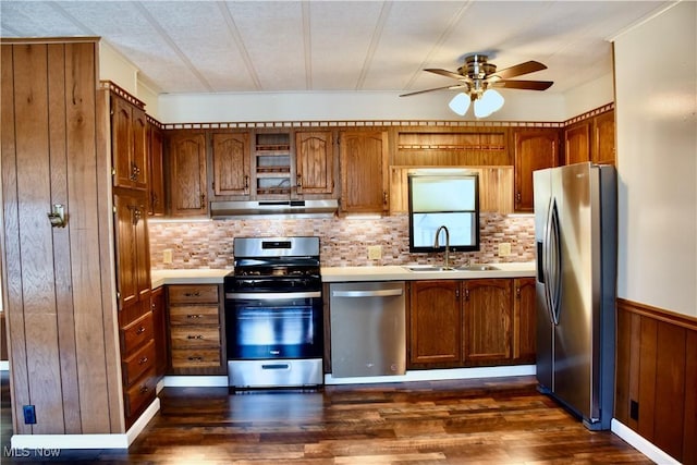 kitchen featuring wood walls, ceiling fan, stainless steel appliances, dark wood-type flooring, and sink