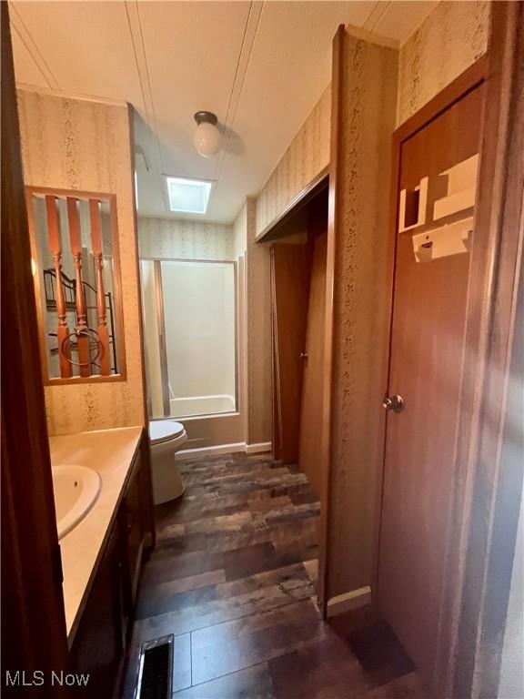 bathroom featuring toilet, vanity, wood-type flooring, and a skylight