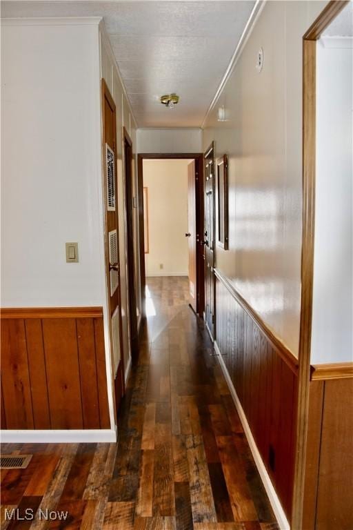 hallway with dark hardwood / wood-style floors, ornamental molding, and wood walls