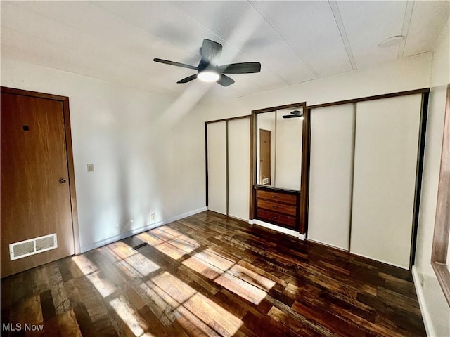 unfurnished bedroom with ceiling fan, dark hardwood / wood-style floors, and multiple closets